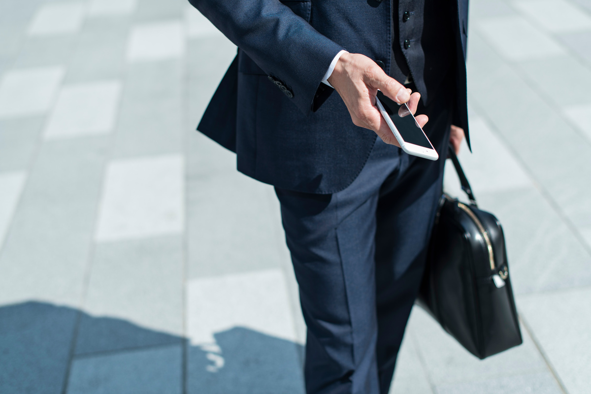 シニア ビジネスマンがスマートフォンを持って街を歩いている