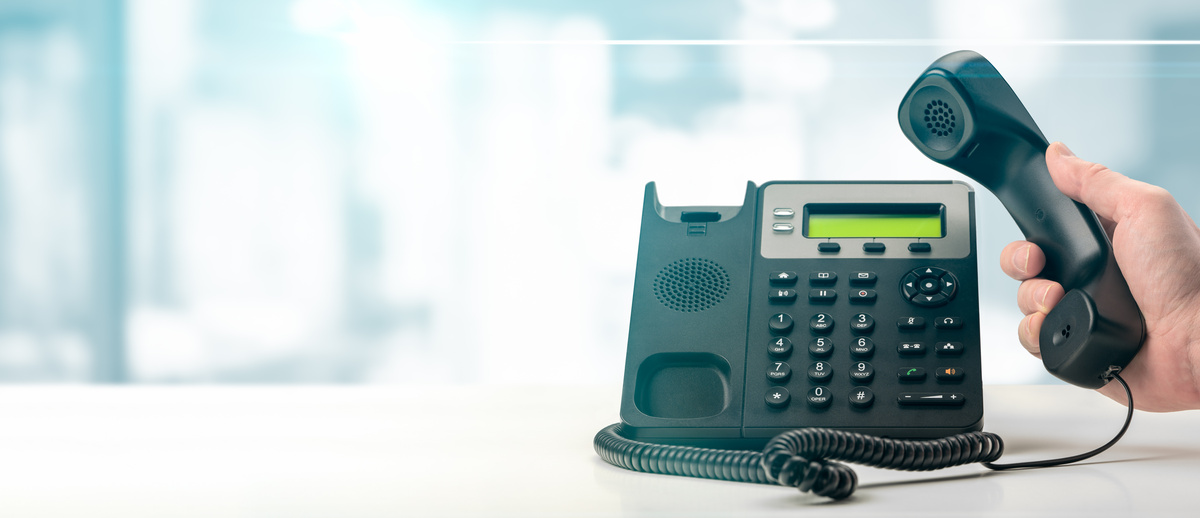 オフィス背景に受話器が上げられた黒いオフィス用固定VOIP電話がテーブルに置かれている。