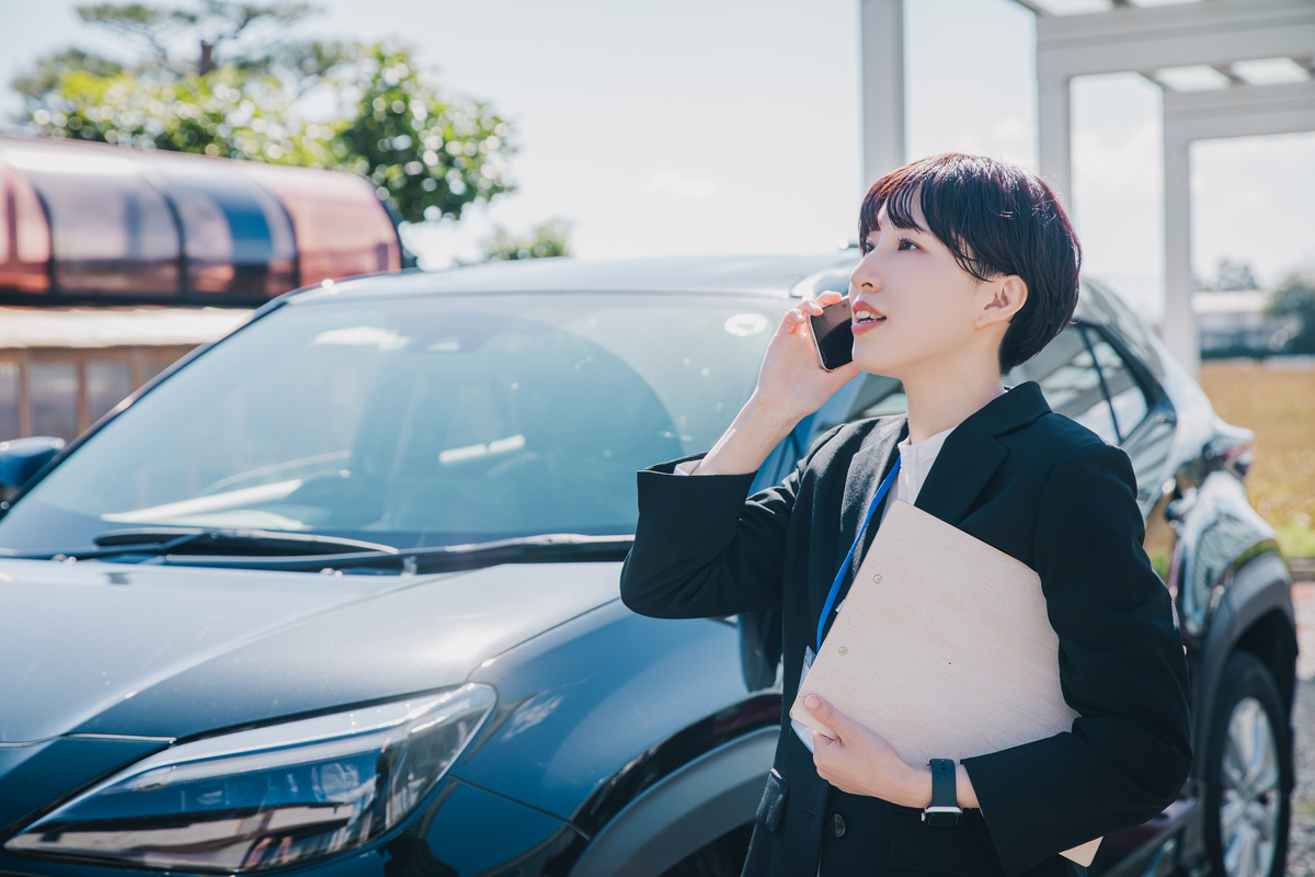 外回り用の車の前で電話する女性営業マン